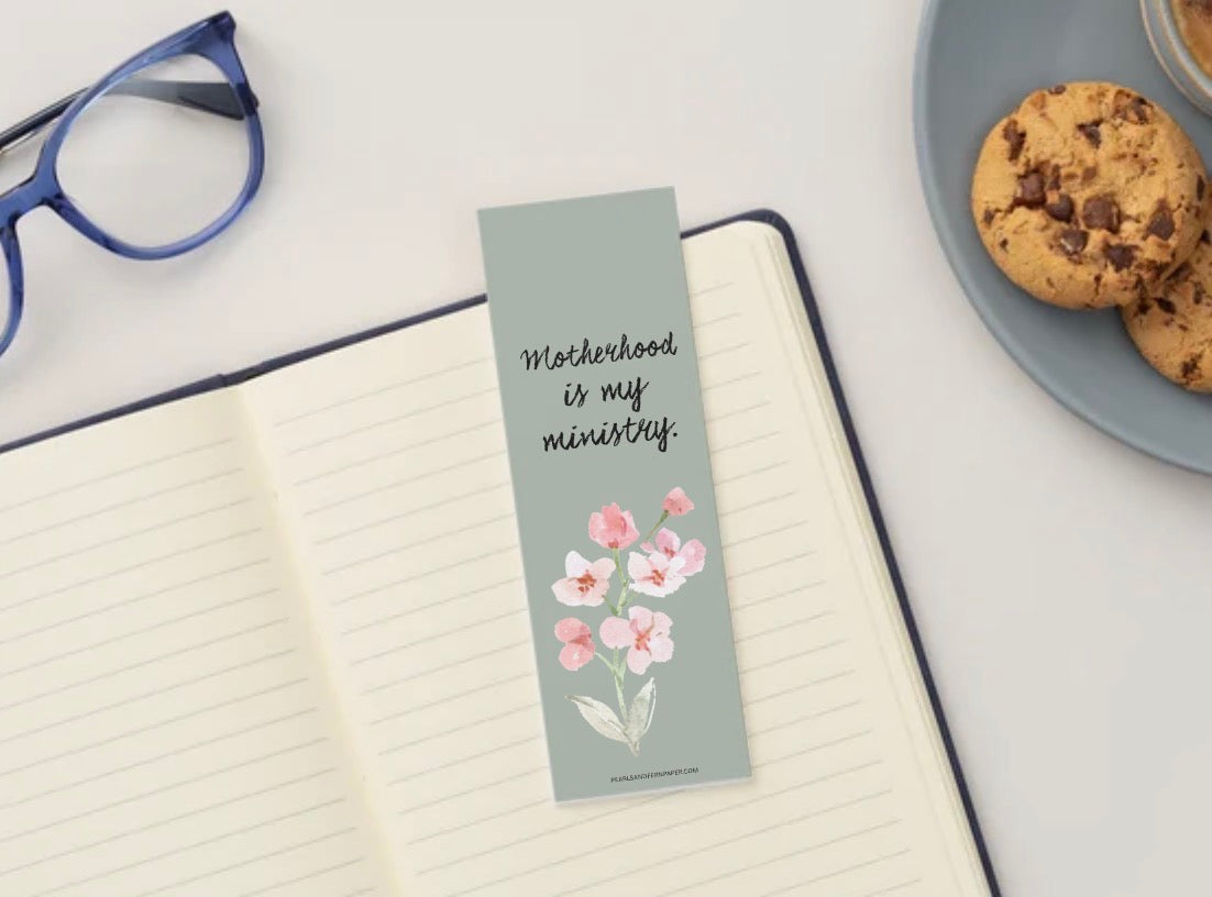 “Motherhood Is My Ministry” bookmark featuring an inspirational faith-based message for Christian mothers and women on top of blank journal. 